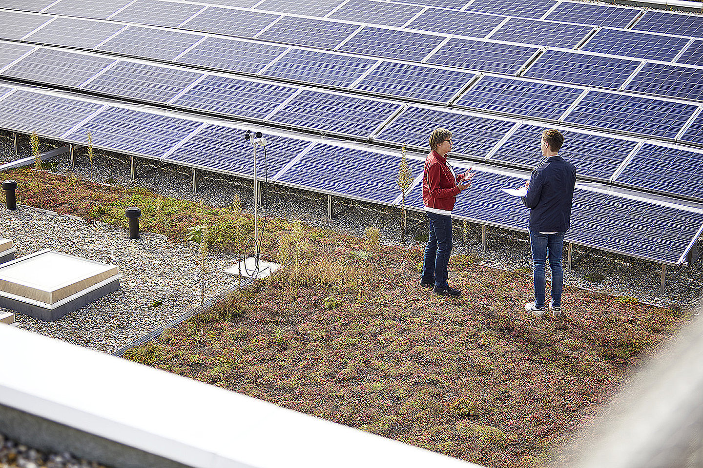 Zwei Personen unterhalten sich auf einem Dach vor einer PV-Anlage