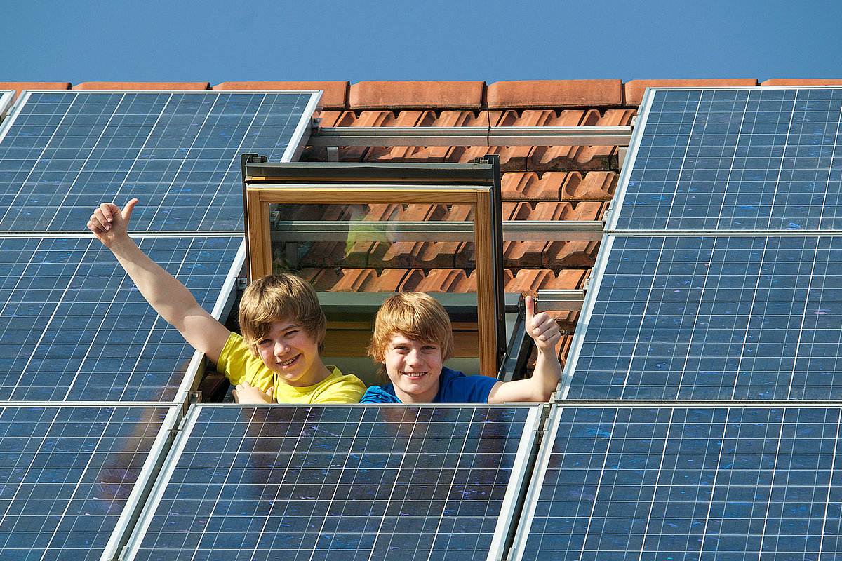 zwei Kinder gucken aus Dachfenster neben Photovoltaikmodulen