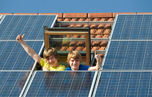 zwei Kinder gucken aus Dachfenster neben Photovoltaikmodulen