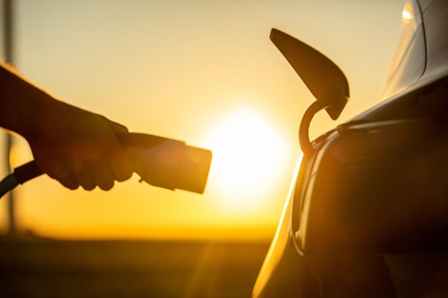 Person hält Ladekabel neben Fahrzeug vor Sonne