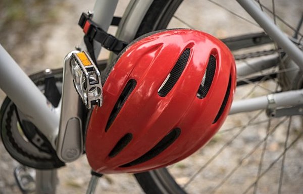 Ausschnitt silberner Fahrradrahmen und Tretlager mit am Rahmen befestigtem roten Helm