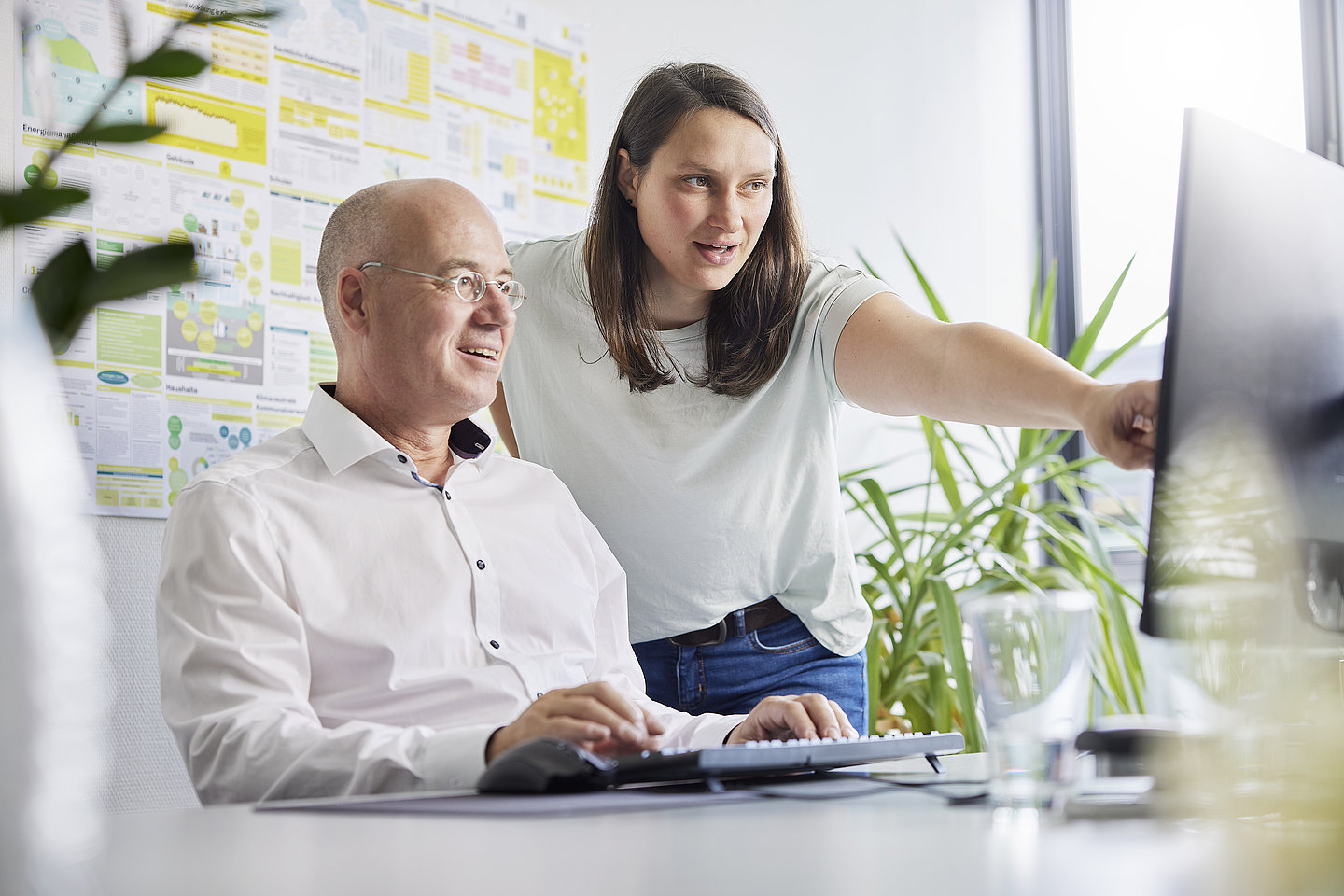 Mann sitzt vor PC, Frau steht daneben und zeigt auf den Bildschirm
