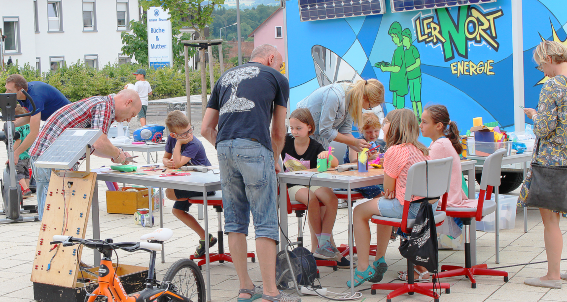 Foto zeigt von Lehrern betreute, bastelnde Kinder. Im Hintergrund der Kinder ist eine bemalte Wand mit der Aufschrift: "Lernort Energie" zu sehen.