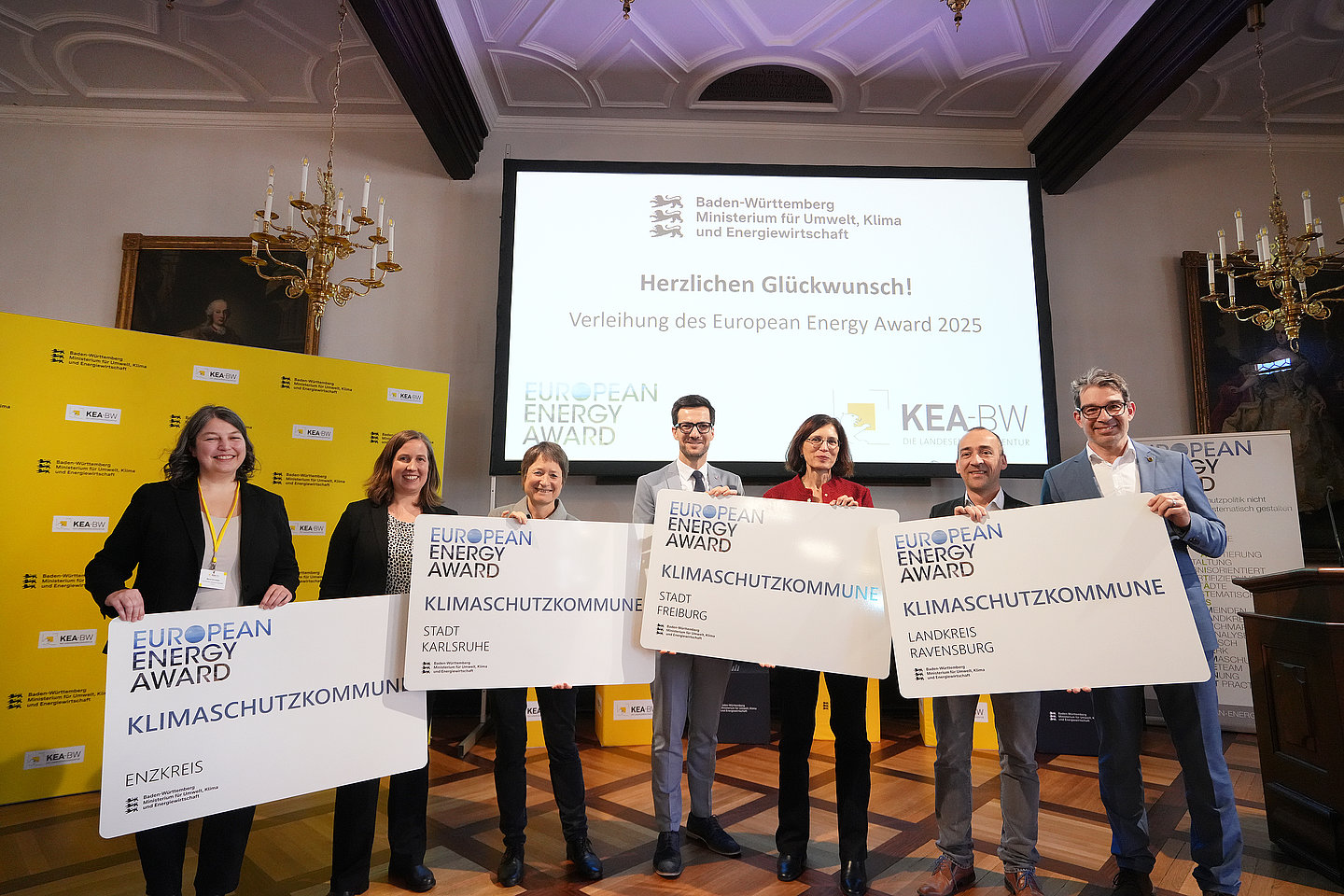 mehrere Personen stehen nebeneinander auf einer Bühne und halten das Schild European Energy Award hoch