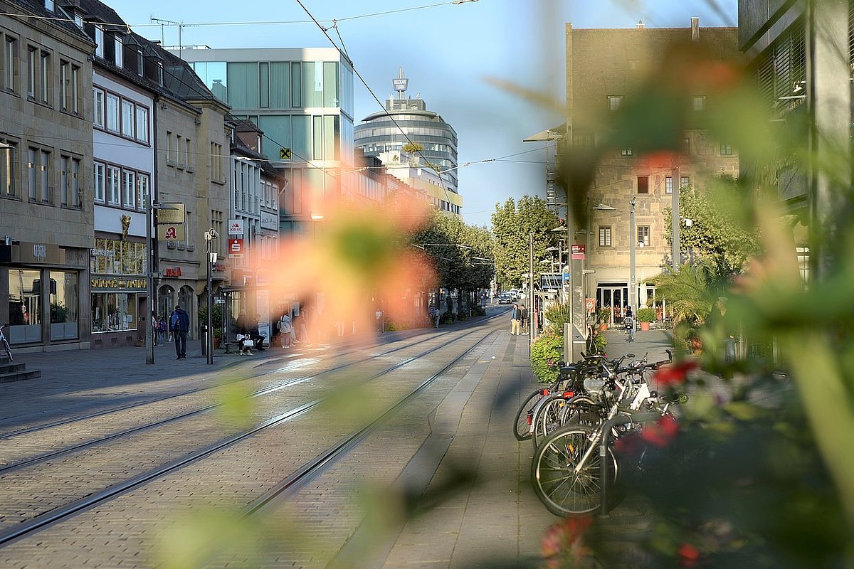 Ansicht einer sonnenbeschienenen Straße, links führen Straßenbahnschienen entlang, rechts auf dem Gehsteig sind Fahrräder abgestellt.  