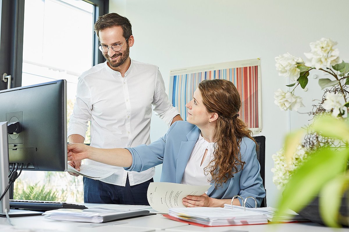 Ein Mann und eine Frau schauen auf einen Computerbildschirm, während sie zusammenarbeiten oder Informationen überprüfen