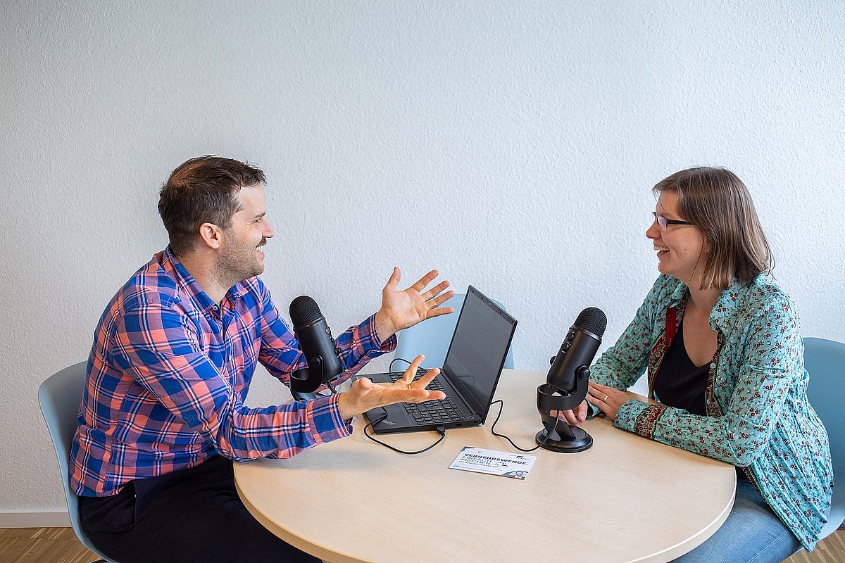 Zwei Personen sitzen an einem Tisch und nehmen einen Podcast auf