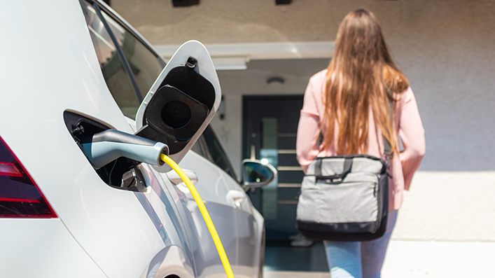 E-Auto mit Ladekabel, Frau von hinten