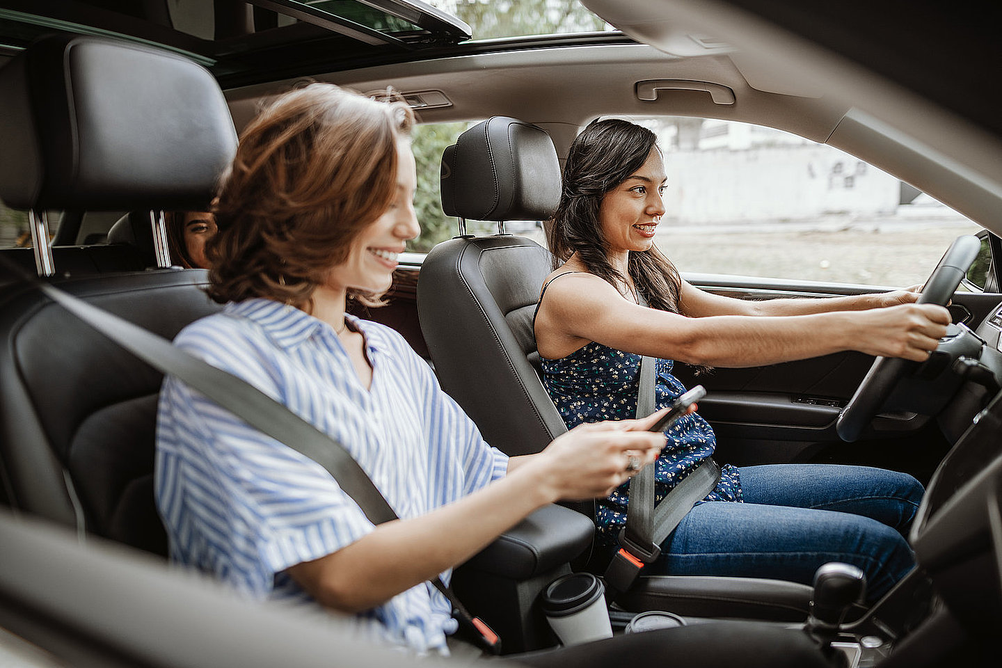 Foto von mehreren Frauen in einem Pkw, alle lächeln. Die Beifahrerin hält ein Smartphone, die Fahrerin hält mit beiden Händen das Lenkrad. Im Fond ist eine weitere Person, die man nur schemenhaft sieht. Foto: iStock/Drazen_