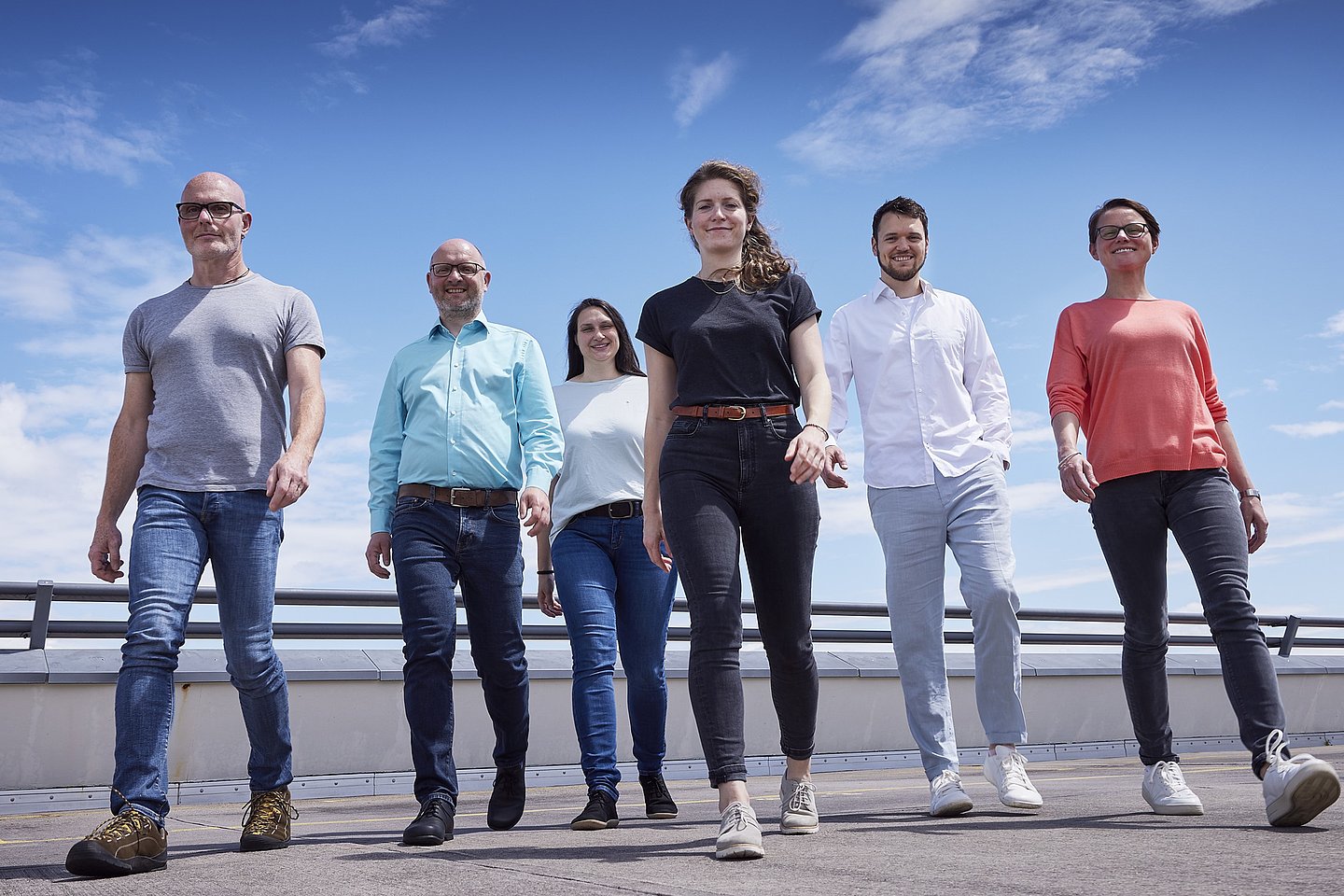 sechs personen gehen auf den Fotografen zu, blauer Himmel