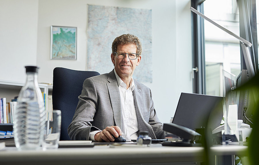 Man sitzt am Schreibtisch und schaut in die Kamera