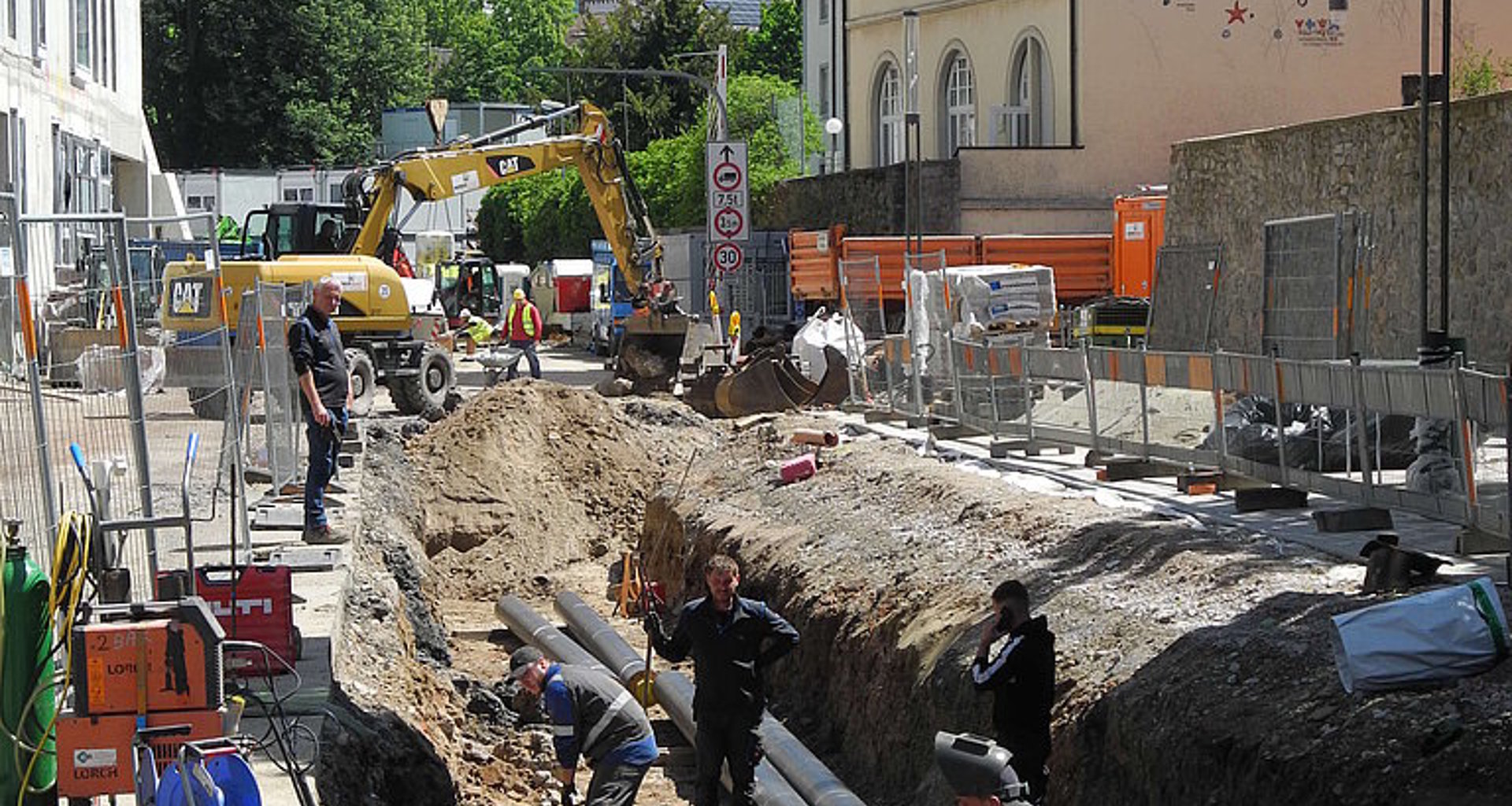 Foto zeigt die Bauarbeiten zur Verlegung der Fernwärmeleitung. Man sieht eine offene Straße und Bauarbeiter.