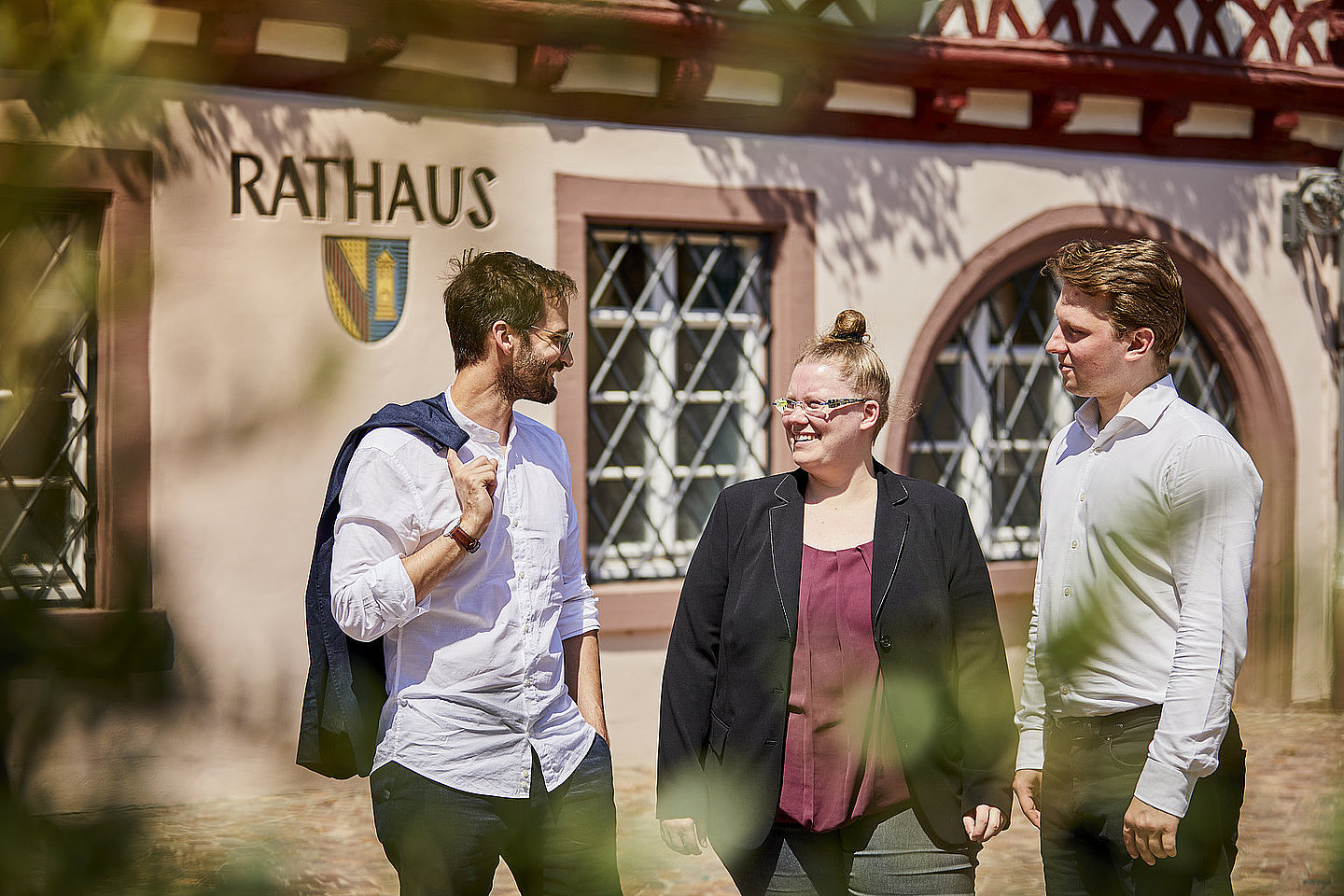 Eine Gruppe von personen unterhält sich vor einem Gebäude mit der Aufschrift "Rathaus"