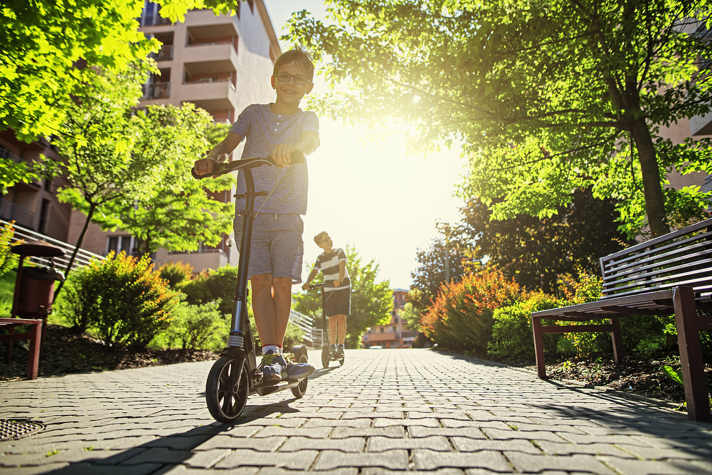 Kinder fahren auf einem Elektroroller durch eun schön begrüntes Wohngebiet