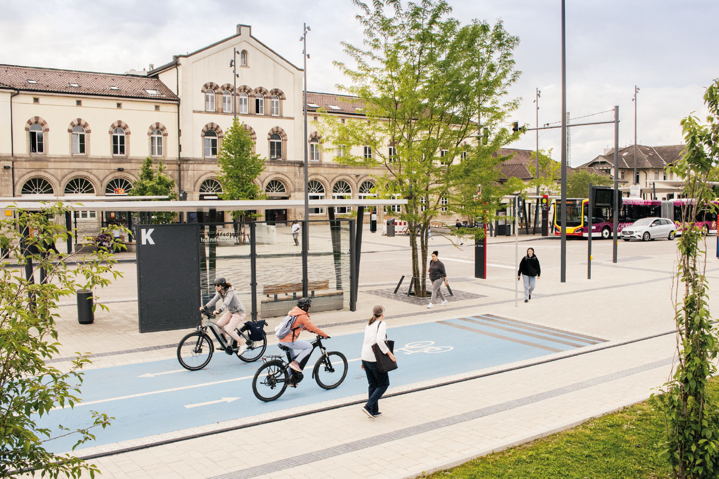 Szene auf Marktplatz mit Fuß- und Radverkehr sowie Auto und Bus im Hintergrund