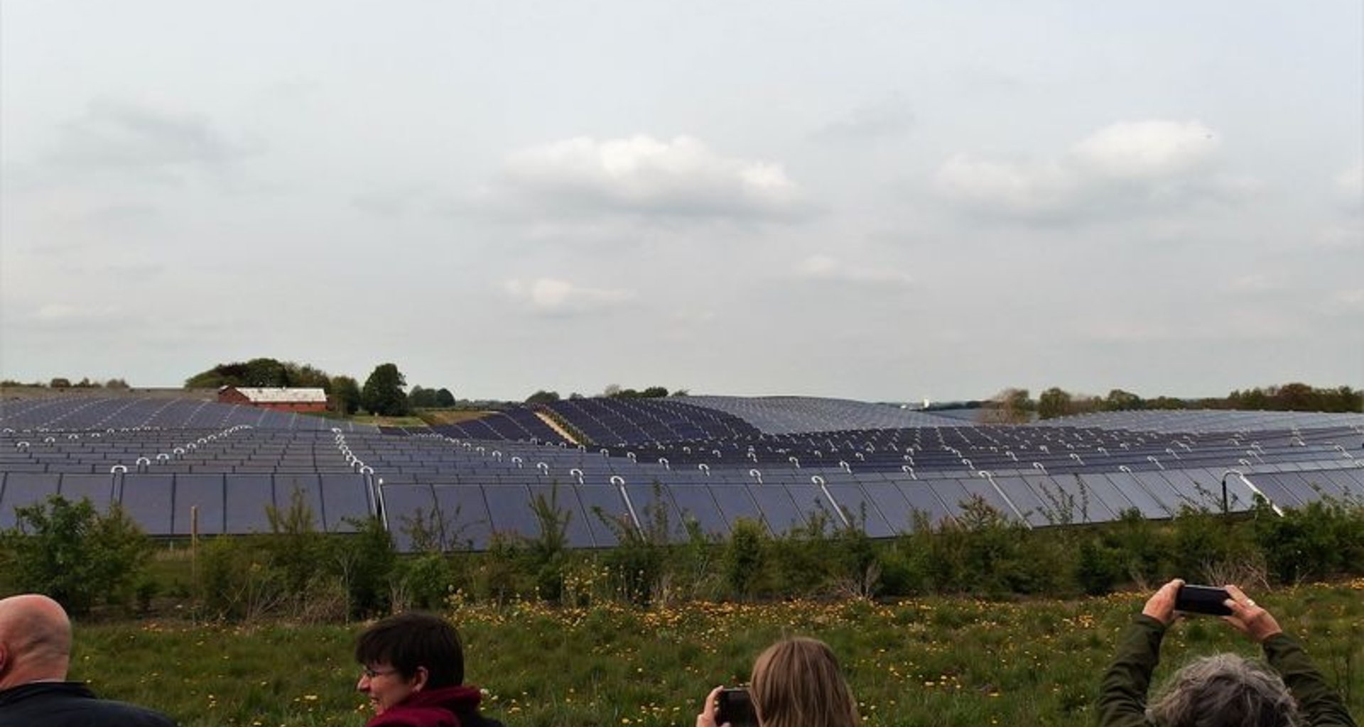 Menschen machen Fotos einer großen Freiflächen-Solarthermieanlage mit Flachkollektoren.