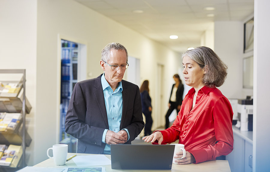 Mann und Frau unterhalten sich vor Laptop in einem Büro-Entree