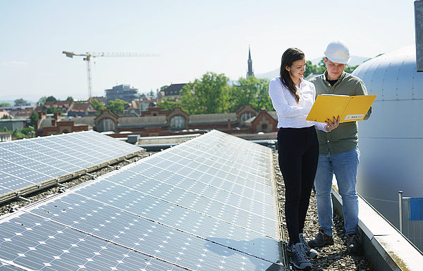 Frau und Mann stehen auf einem Dach mit Photovoltaik und unterhalten sich