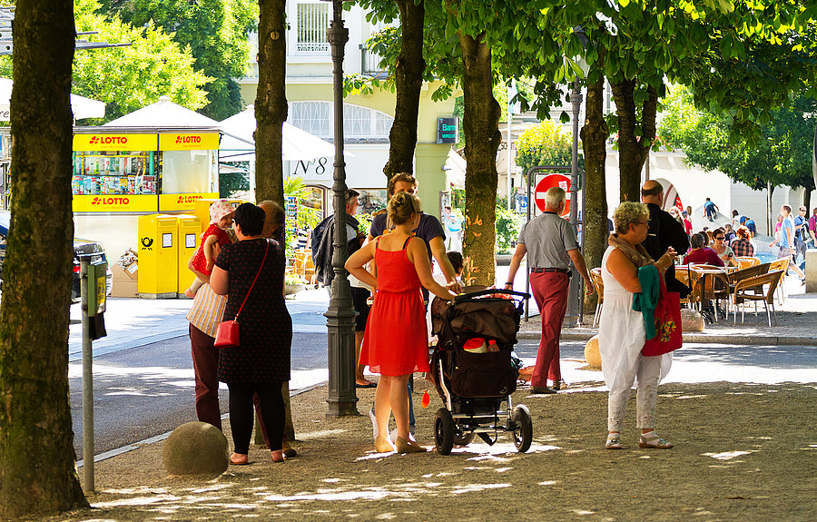 Menschen stehen unter Bäumen in verkehrsberuhigter Zone