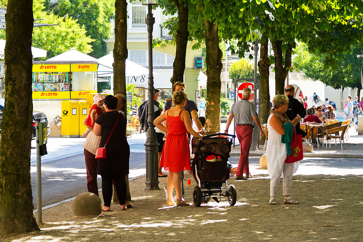 Menschen stehen unter Bäumen in verkehrsberuhigter Zone
