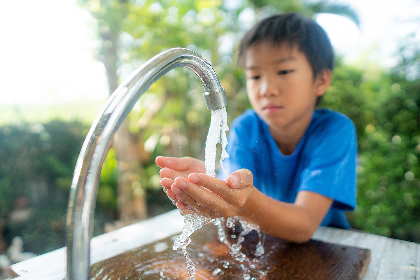 Junge wäscht seine Hände an einem Wasserhahn im Garten