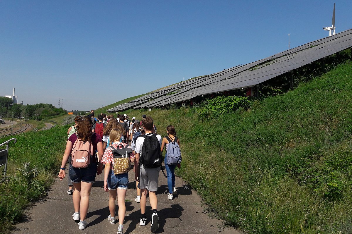 eine Gruppe von Schülerinnen und Schülern gehen auf einen mit Photovoltaik bestückten Hügel