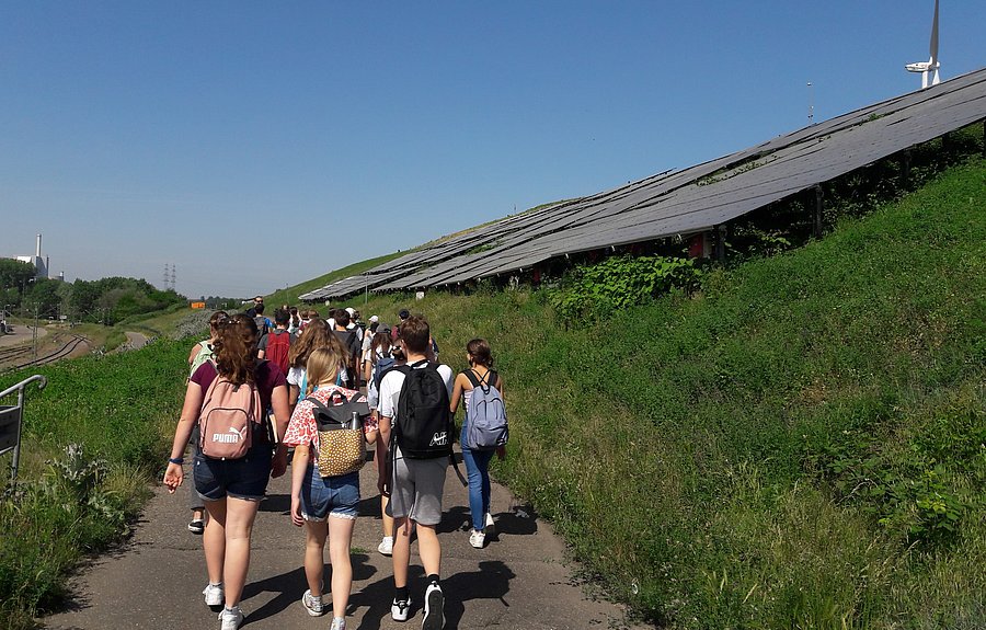 eine Gruppe von Schülerinnen und Schülern gehen auf einen mit Photovoltaik bestückten Hügel