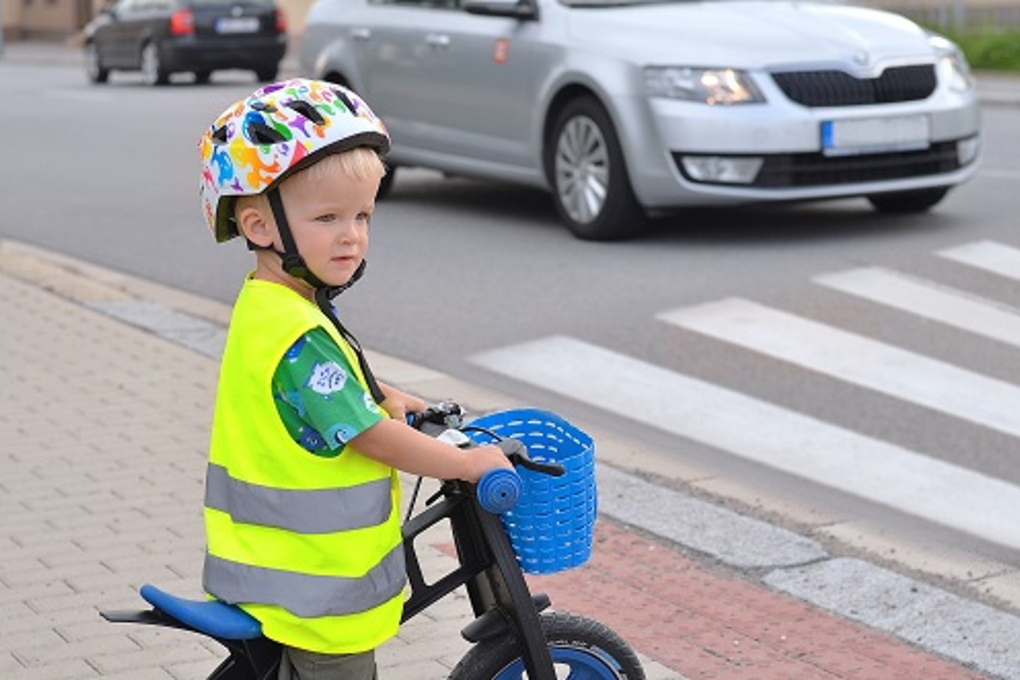 Vorschulkind mit Fahrradhelm und Fahrrad vor Zebrastreifen und Auto