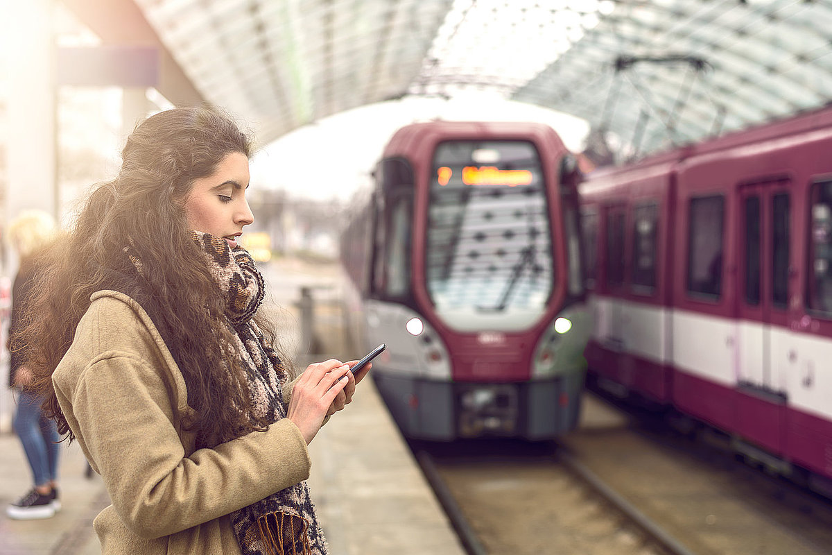 Frau steht an der Haltestelle und schaut aufs Handy