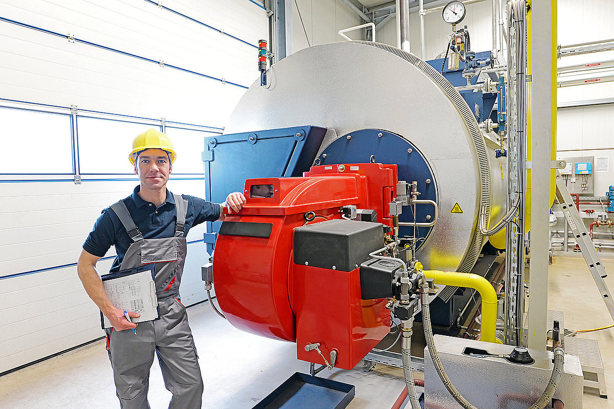 Ein Handwerker in grauer Kleidung steht vor einer Industrieanlage