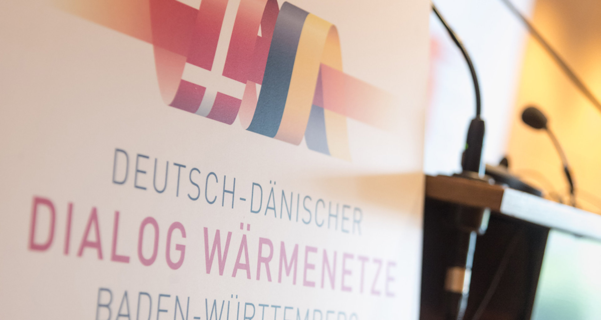 Aufsteller mit der Aufschrift "Deutsch Dänischer Dialog Wärmenetz Baden-Württemberg" neben einem Rednerpult.