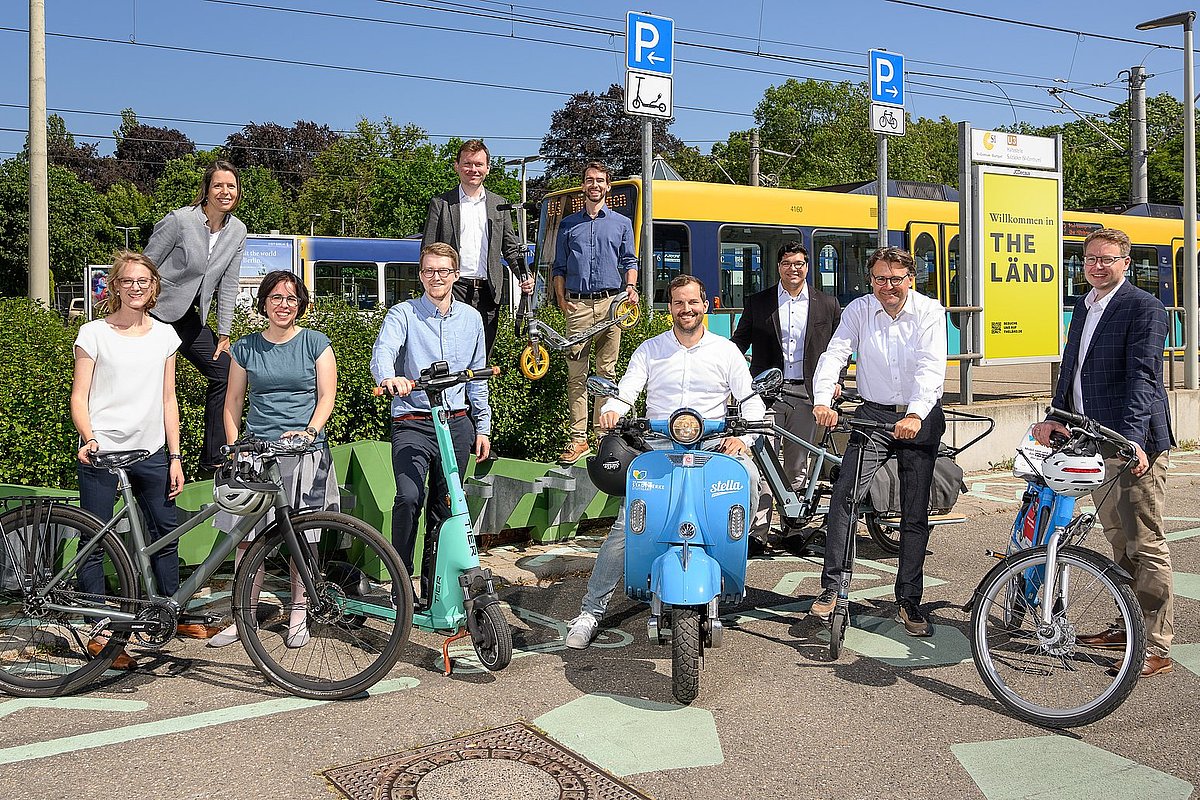 mehrere personen stehen mit Elektrofahrzeugen vor einem Bahnsteig