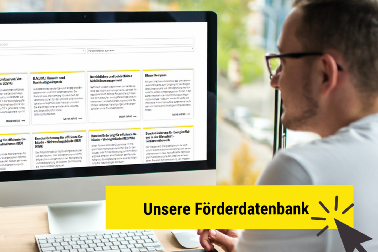 Mann sitzt vor einem Bildschirm und schaut sich die Förderdatenbank an.