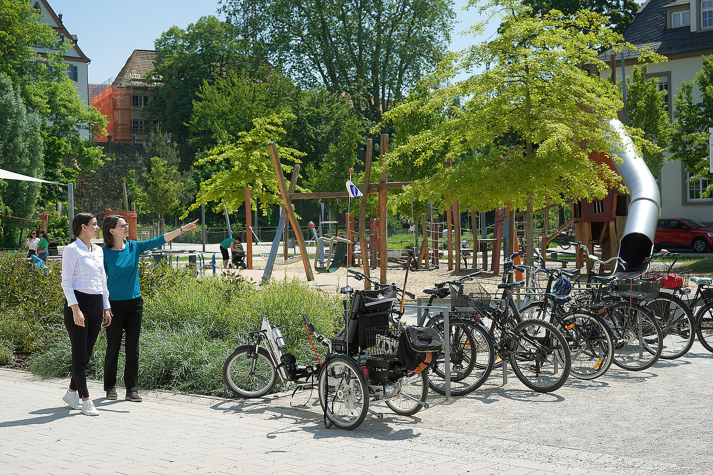 Zwei Frauen gehen an einem Spileplatz spazieren, daneben Fahrradständer