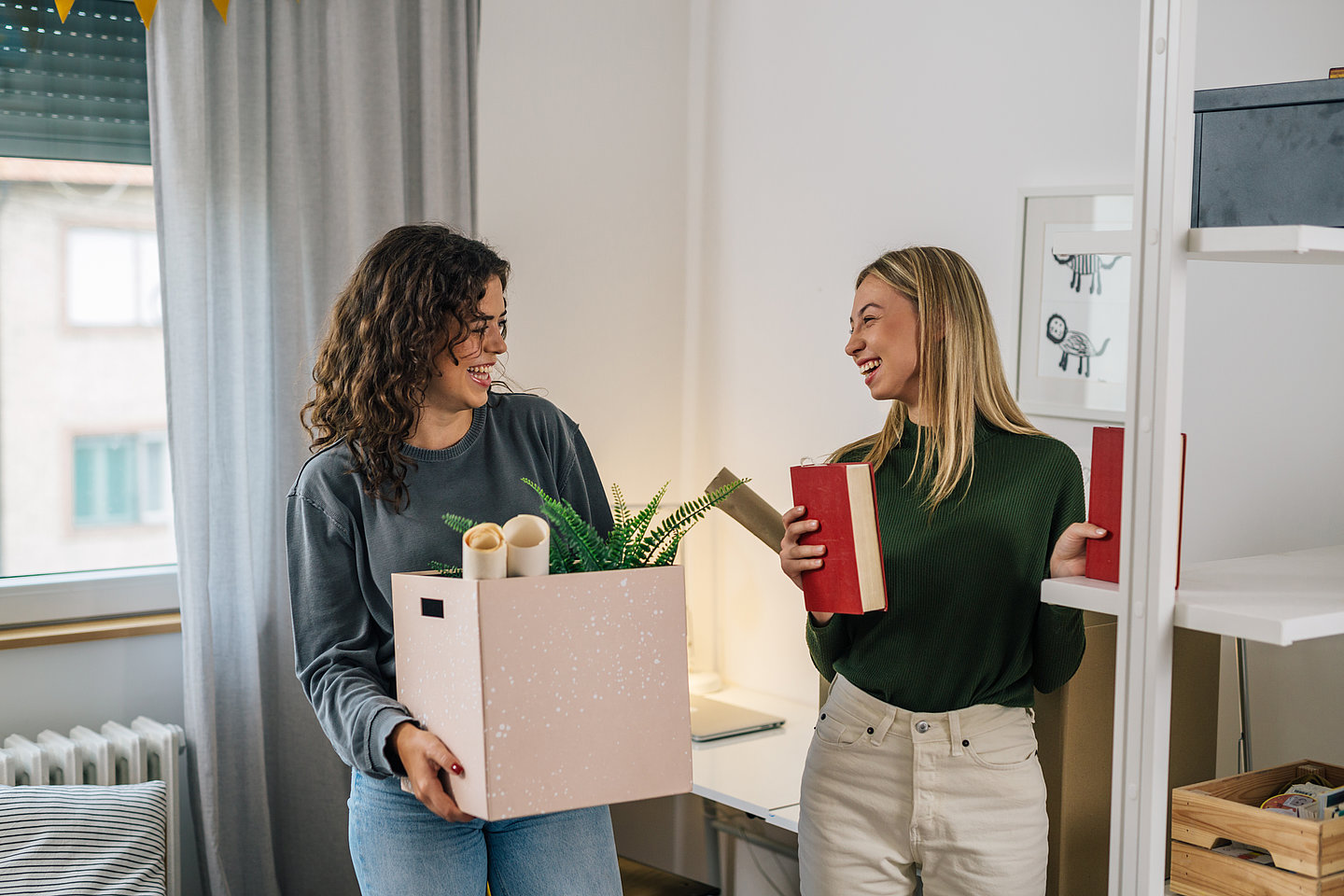 zwei junge Frauen mit umzugskartons in einem kleinen Zimmer
