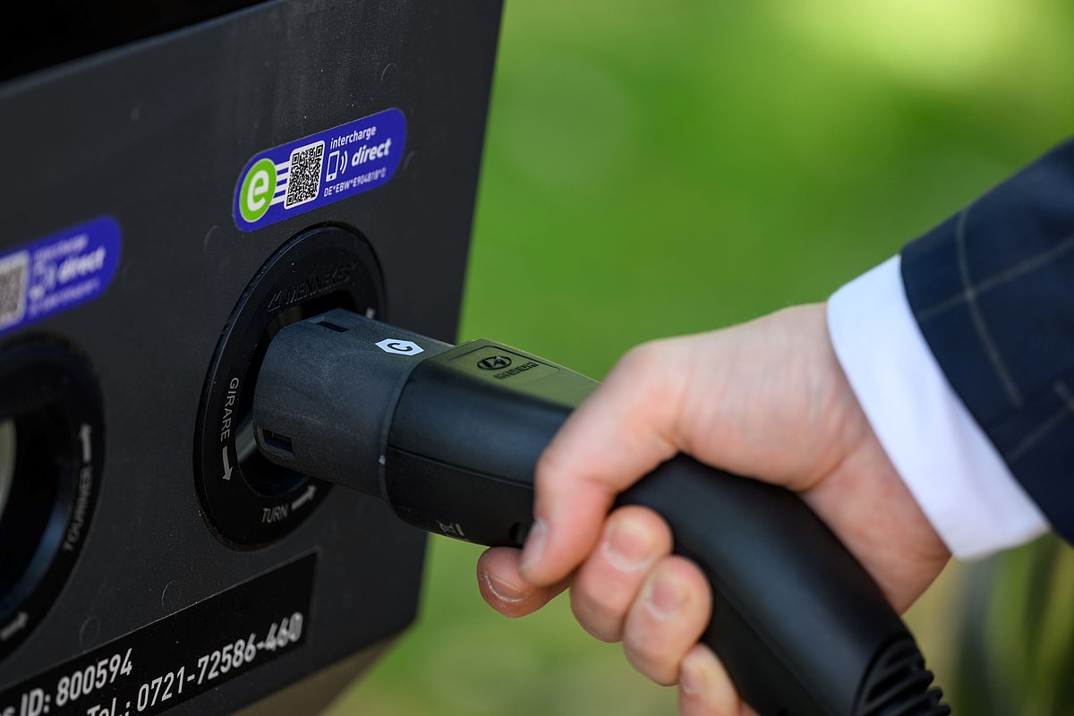 Hand steckt E-Auto-Ladekabel in Ladesäule
