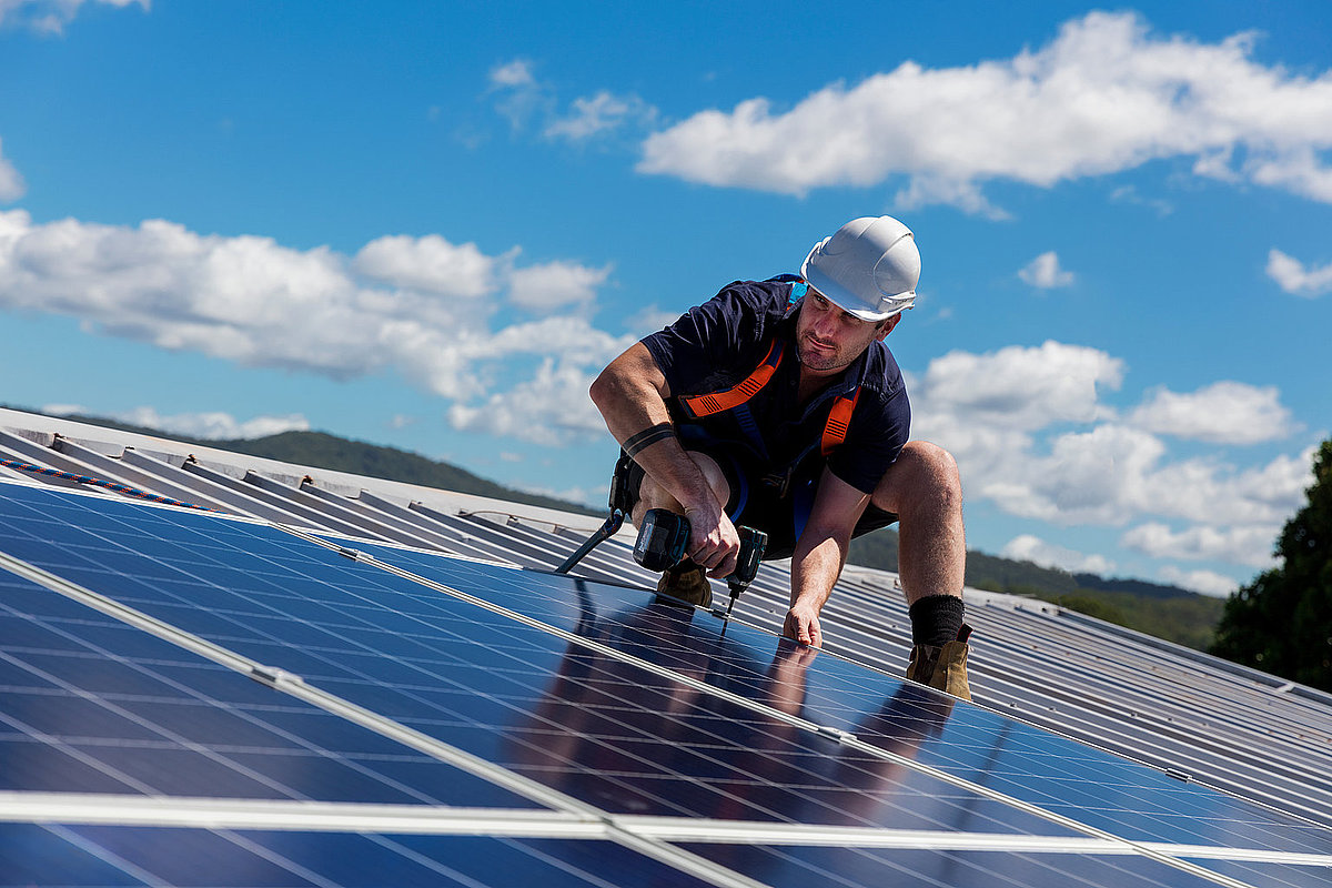 Mann montiert PV-Anlage auf Dach