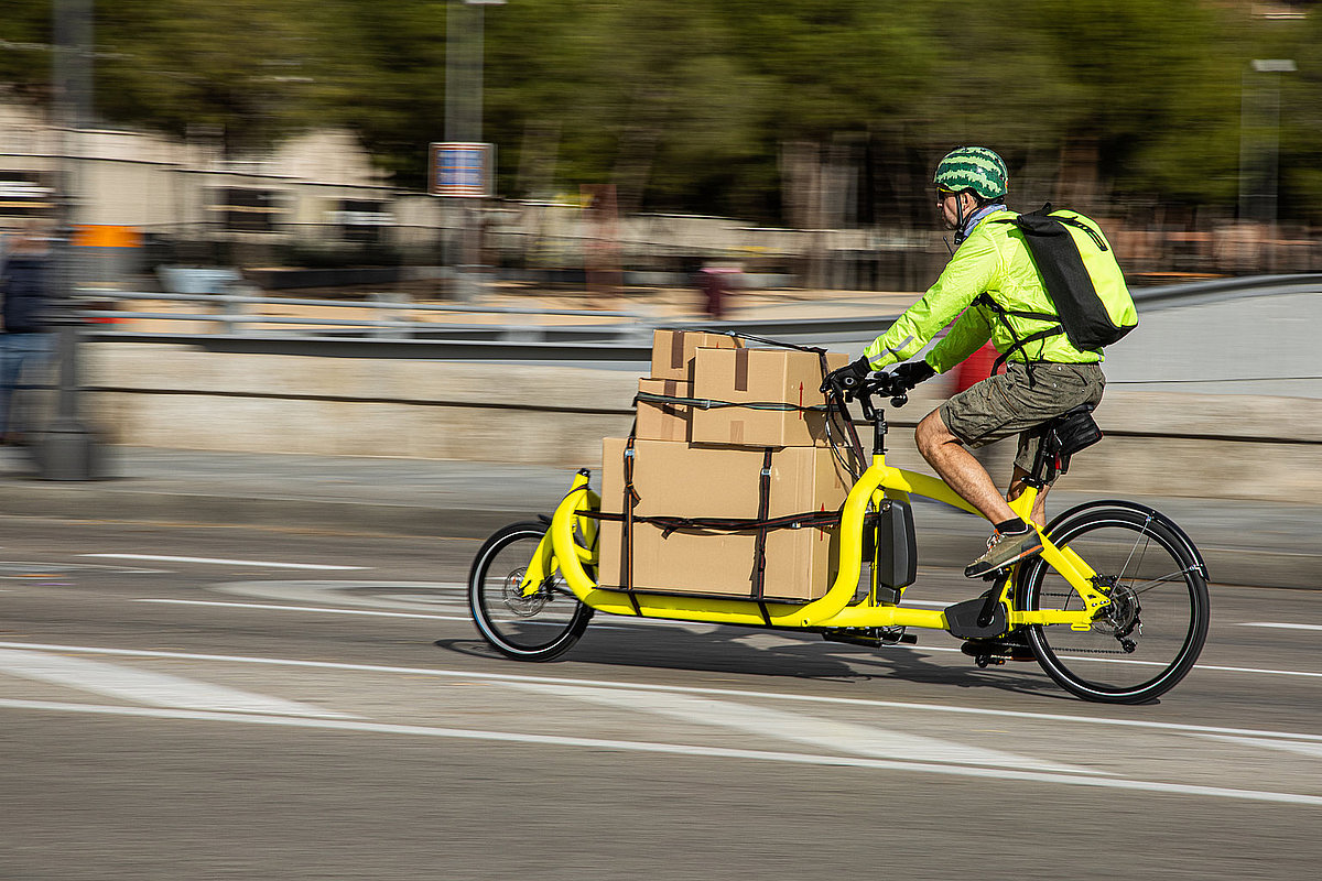 Fahrer mit grünem Helm und gelbem Lastenrad und Paketen in Stadt