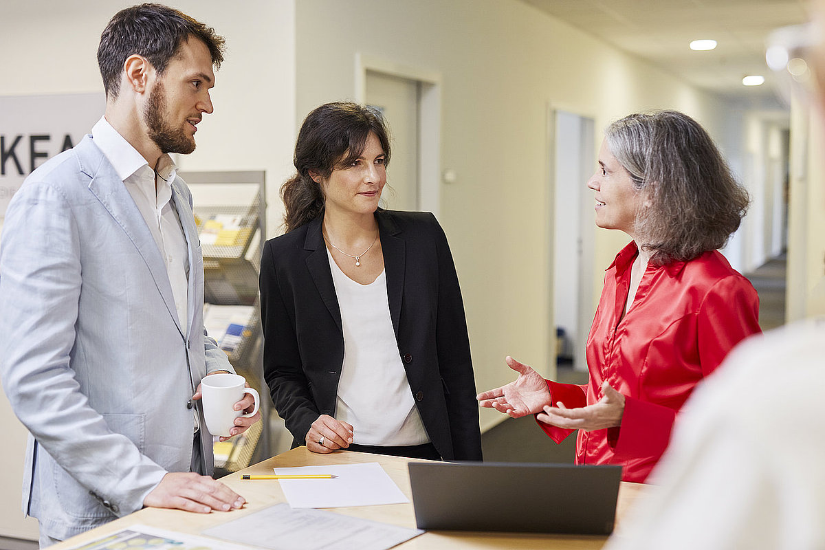 Ein Mann und zwei Frauen unterhalten sich in einem Büroflur