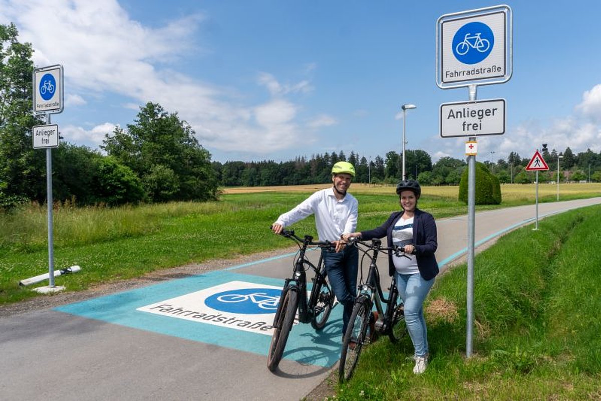 2 Menschen mit Fahrrädern vor beschilderter und markierter Fahrradstraße