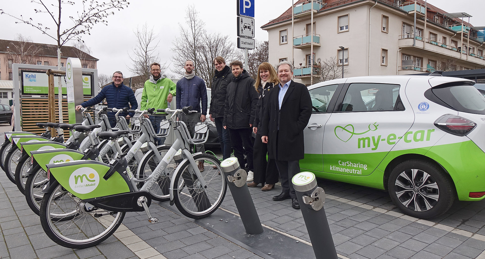 Sieben Personen stehen vor einer Mobilstation mit Fahrrädern und E-Carsharing in Kehl