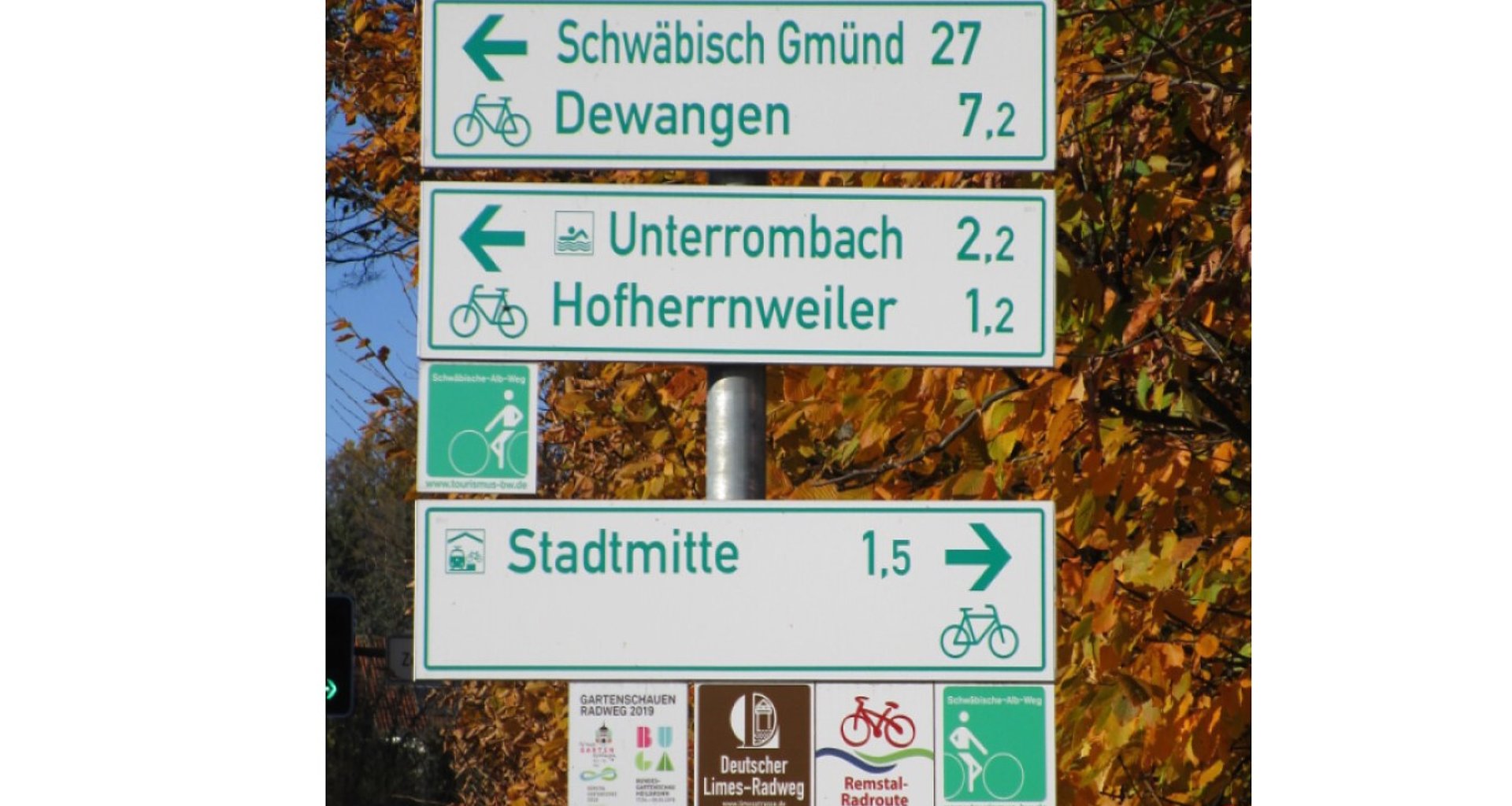 Foto einer Wegweisersäule mit drei Schildern und mehreren gekennzeichneten Routen.