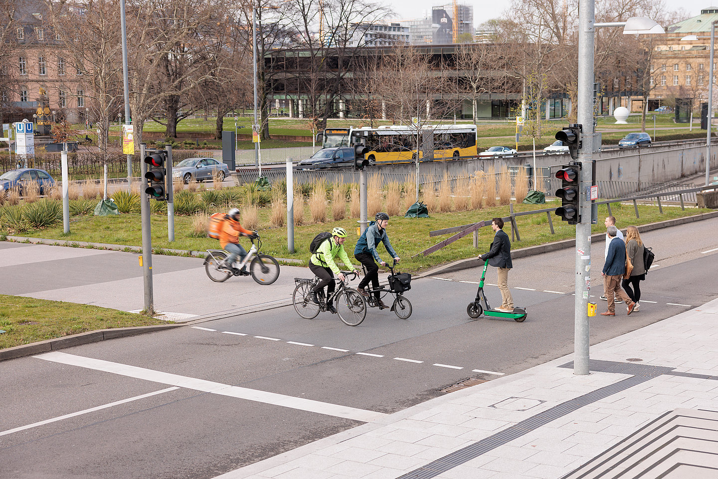 Menschen queren Ampel zu Fuß, per Rad und Roller vor dem Stuttgarter Landtag, Bus und Pkw im Hintergrund