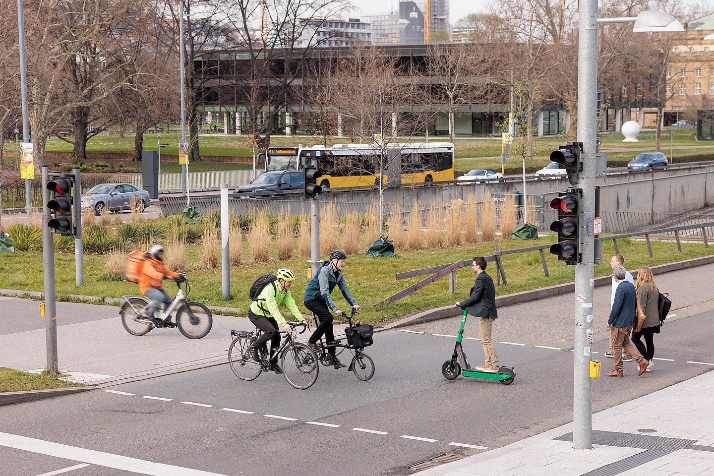 Menschen queren Ampel zu Fuß, per Rad und Roller vor dem Stuttgarter Landtag, Bus und Pkw im Hintergrund