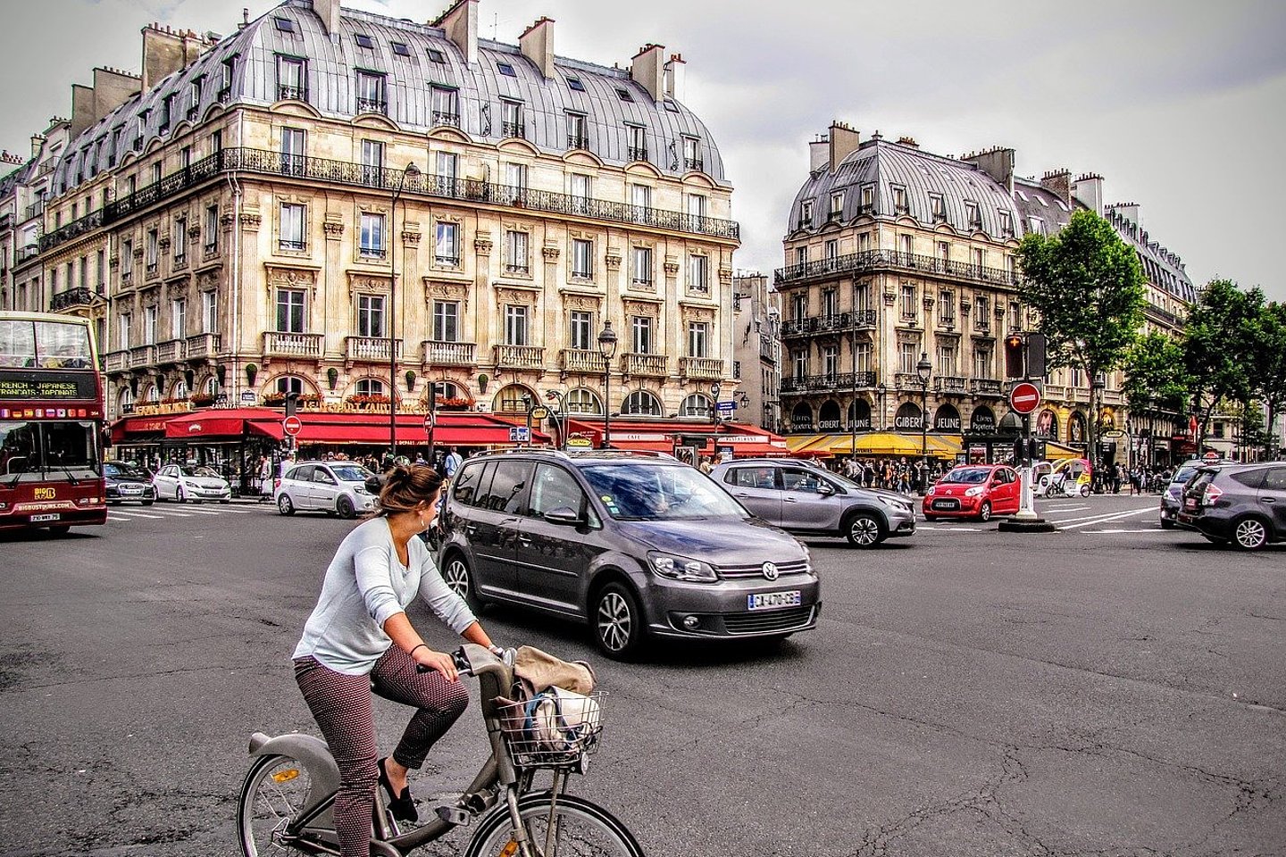Stadtverkehr in Paris an einer Kreuzung. Fahrradfahrerin, Autos, Busse, Passanten