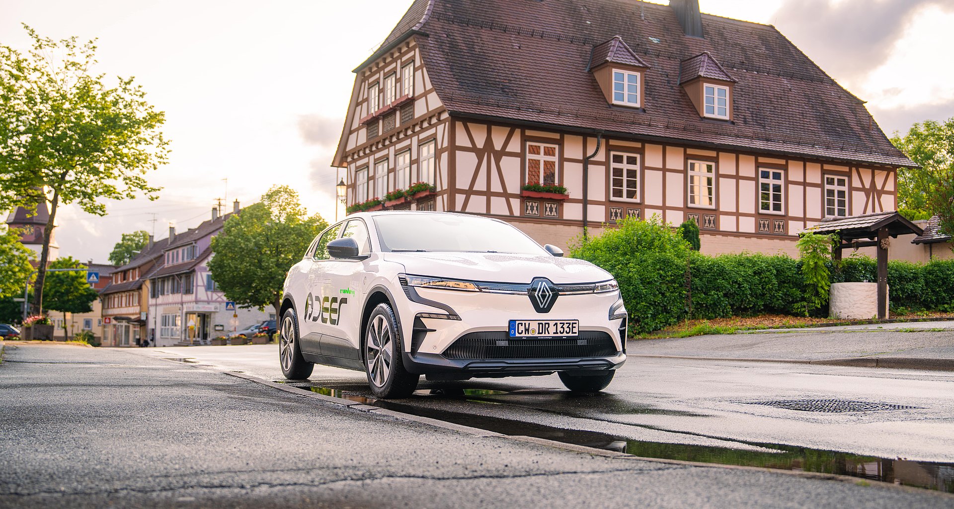 Ein weißes deer Carsharing Fahrzeug auf einer Straße vor einem Haus
