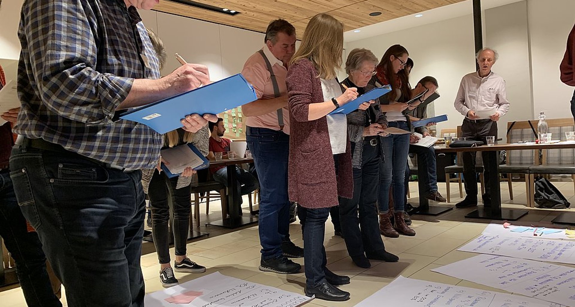 Klimakommission bei der Arbeit. Eine Reihe Menschen schreibt im stehen auf Klemmbrettern.