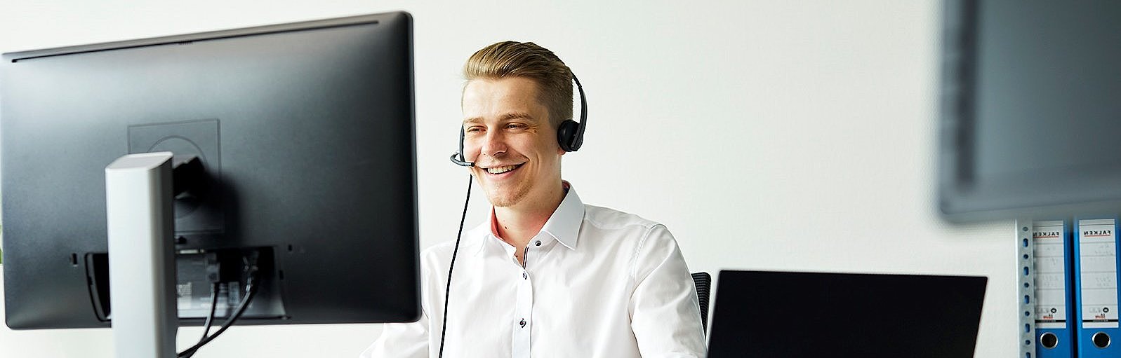 Mann sitzt mit Headset vor dem Computer