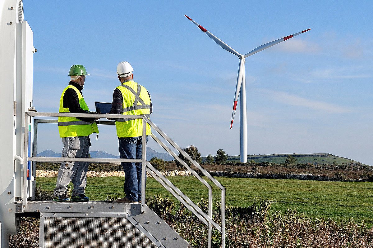 Zwei Männer stehen an einer Windkraftanlage und schauen auf ein Windrad