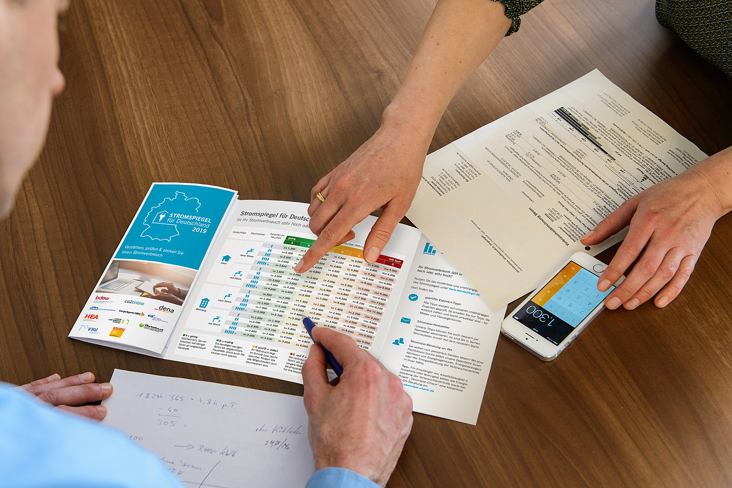 auf einem tisch liegt eine rechnung und ein taschenrechner, drei Hände sind zu sehen